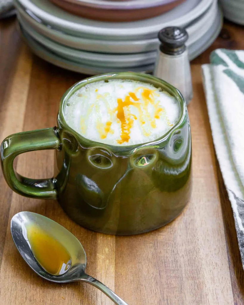 A salted honey latte in a mug with a honey drizzle on top. There is a spoon next to the mug with honey on it.